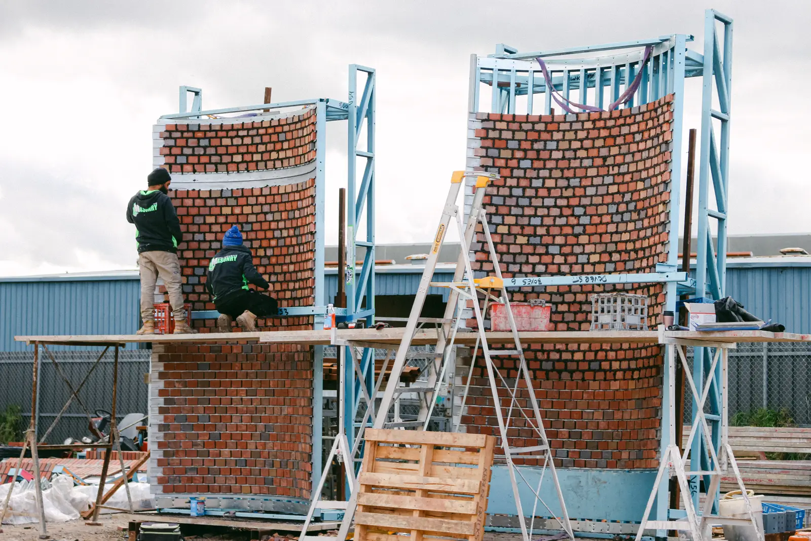 Installers building curved real brick facade panels on steel rail frames at Dova Street