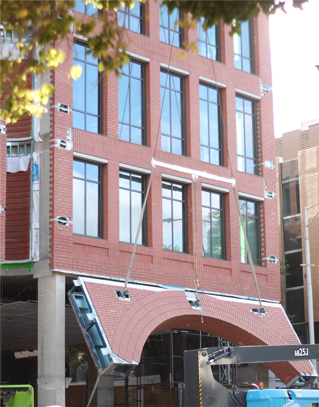 Installer fixing a cut brick facing panel to a rail system on a building facade